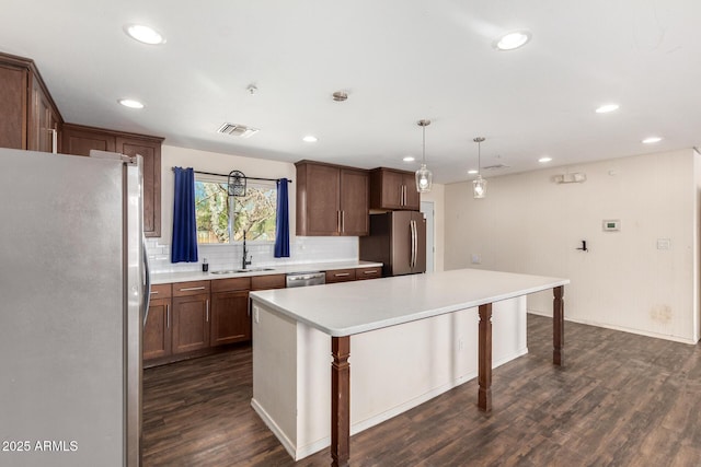 kitchen with appliances with stainless steel finishes, a center island, hanging light fixtures, light countertops, and a sink