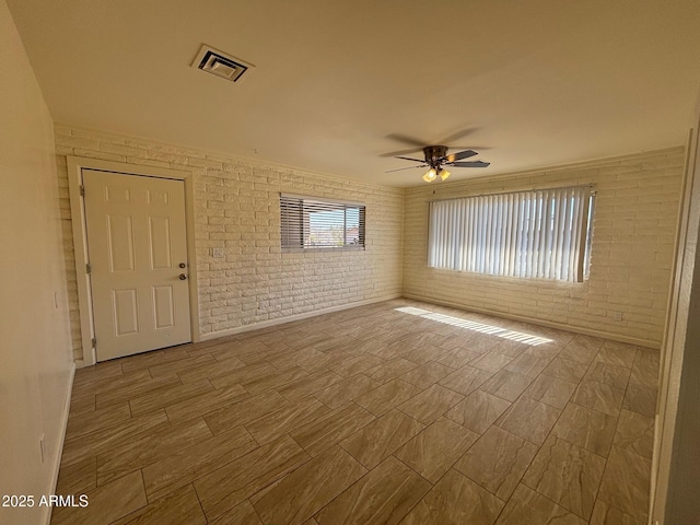 unfurnished room featuring visible vents, brick wall, ceiling fan, and wood tiled floor