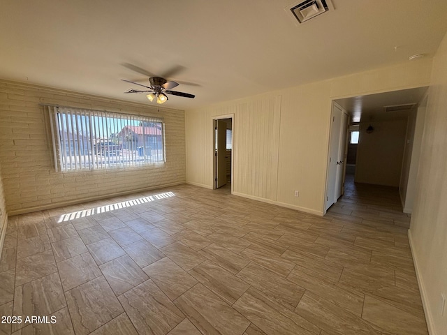 unfurnished room with baseboards, visible vents, brick wall, and ceiling fan