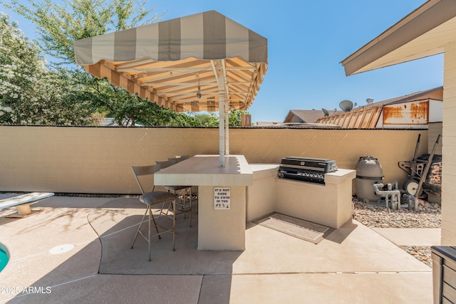 view of patio with an outdoor kitchen, fence, area for grilling, and an outdoor bar