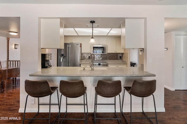 kitchen featuring stainless steel appliances, a sink, a peninsula, and dark wood finished floors