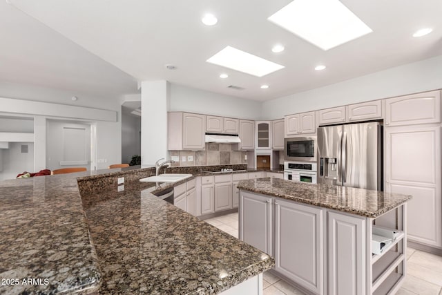 kitchen featuring under cabinet range hood, a sink, appliances with stainless steel finishes, a center island, and tasteful backsplash