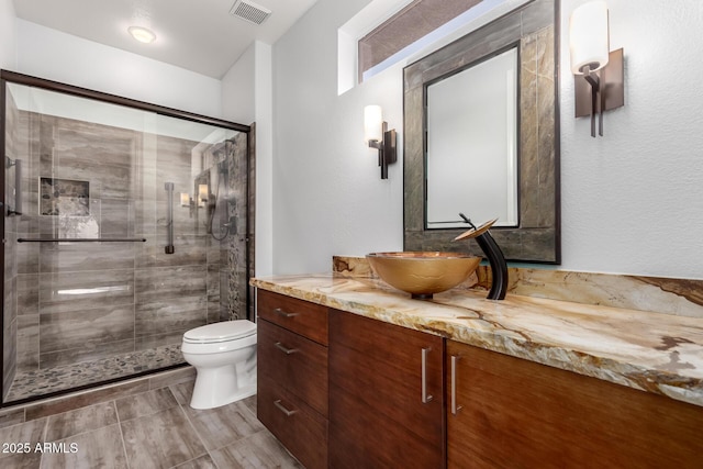 bathroom with visible vents, a shower stall, toilet, and vanity