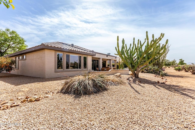 rear view of property with a patio area, a tiled roof, and stucco siding