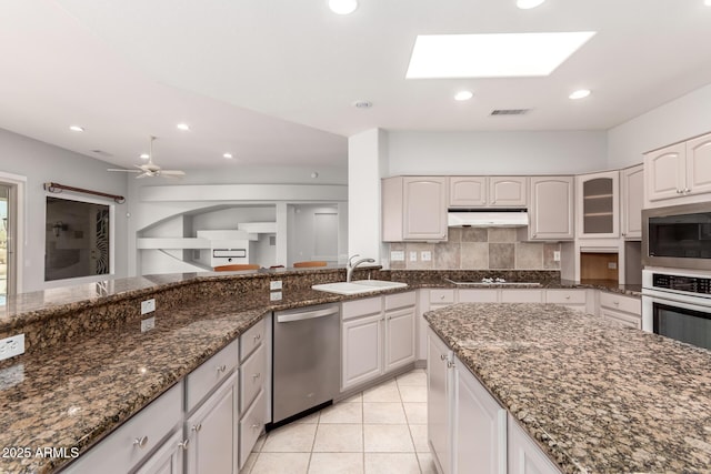 kitchen with tasteful backsplash, appliances with stainless steel finishes, a sink, dark stone counters, and under cabinet range hood