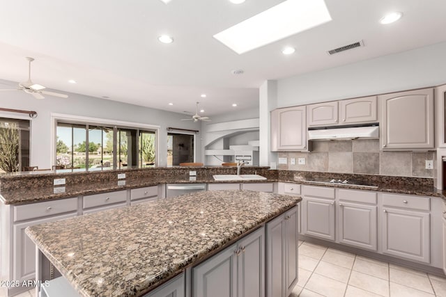 kitchen featuring visible vents, a kitchen island, a sink, ceiling fan, and under cabinet range hood