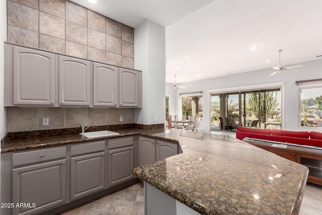 kitchen featuring ceiling fan, a peninsula, a sink, open floor plan, and dark stone counters