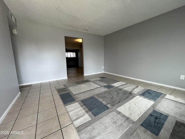 tiled empty room with a textured ceiling and baseboards