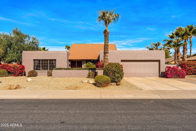 pueblo-style house featuring driveway, a tiled roof, a garage, and stucco siding