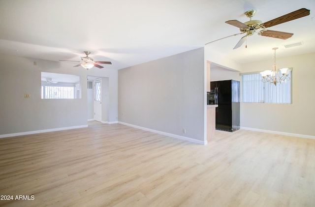 empty room featuring ceiling fan with notable chandelier and light wood-type flooring