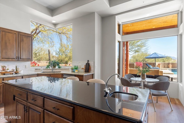 kitchen featuring a center island with sink, sink, tasteful backsplash, and dark stone counters