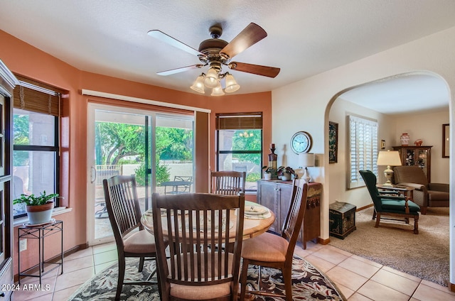 dining area featuring arched walkways, ceiling fan, light tile patterned flooring, and light colored carpet