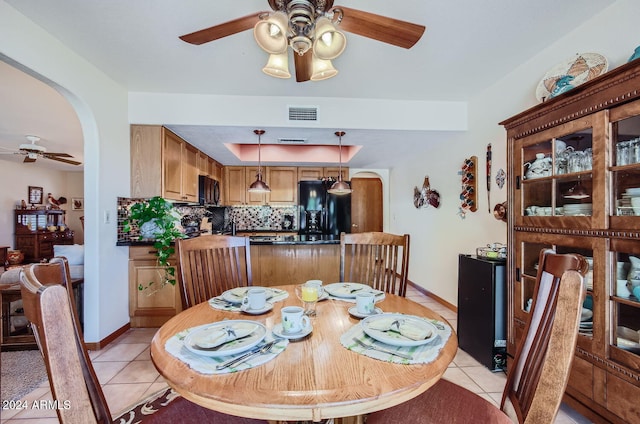 dining space featuring arched walkways, a tray ceiling, visible vents, light tile patterned flooring, and ceiling fan