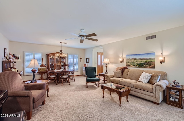 living area with arched walkways, ceiling fan with notable chandelier, visible vents, and light colored carpet