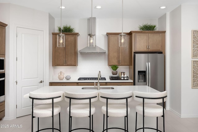 kitchen featuring hanging light fixtures, tasteful backsplash, a center island with sink, stainless steel fridge with ice dispenser, and wall chimney exhaust hood