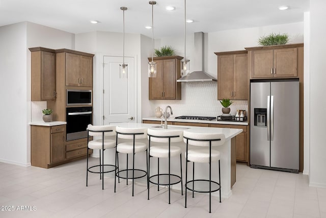 kitchen featuring backsplash, hanging light fixtures, a kitchen island with sink, stainless steel appliances, and wall chimney range hood