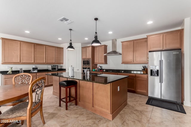 kitchen featuring pendant lighting, wall chimney exhaust hood, dark stone countertops, an island with sink, and appliances with stainless steel finishes