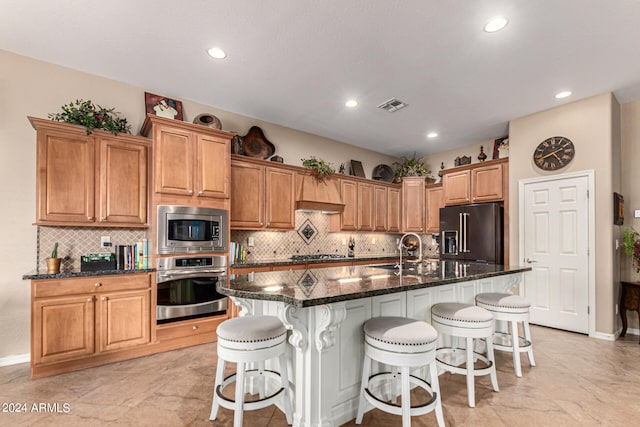 kitchen with a kitchen island with sink, stainless steel appliances, a sink, visible vents, and dark stone counters