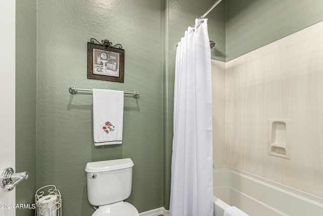 bathroom with a textured wall, shower / tub combo with curtain, and toilet