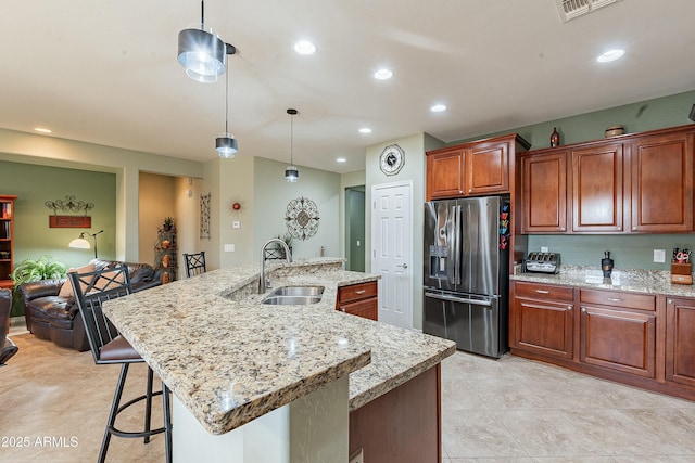 kitchen featuring stainless steel fridge, a center island with sink, a breakfast bar, pendant lighting, and a sink