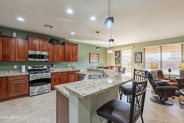 kitchen featuring an island with sink, appliances with stainless steel finishes, a breakfast bar, decorative light fixtures, and a sink