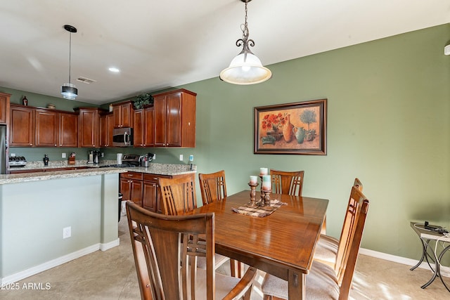 kitchen with appliances with stainless steel finishes, pendant lighting, brown cabinetry, and light stone counters