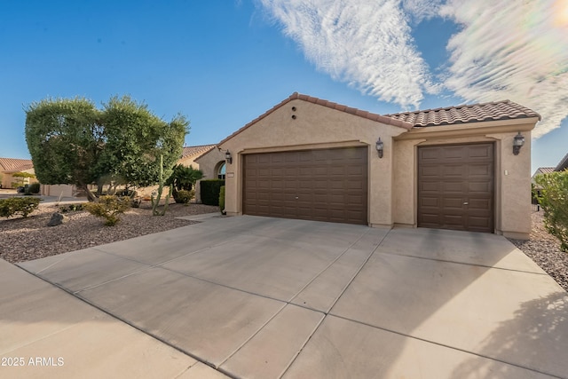 mediterranean / spanish home featuring a garage, a tiled roof, driveway, and stucco siding