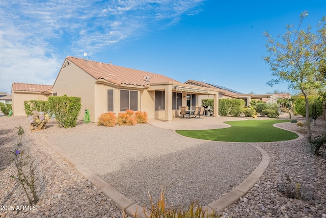 rear view of property with a patio, a lawn, a tile roof, and stucco siding