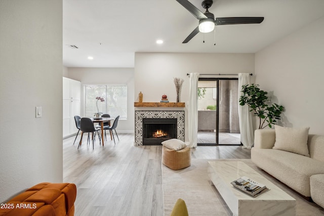 living area featuring healthy amount of natural light, light wood-type flooring, a tiled fireplace, a ceiling fan, and recessed lighting