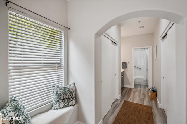 hall featuring arched walkways, light wood-style flooring, and baseboards