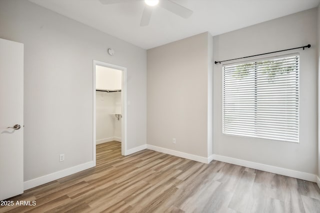 unfurnished bedroom featuring light wood-type flooring, baseboards, a closet, a walk in closet, and a ceiling fan