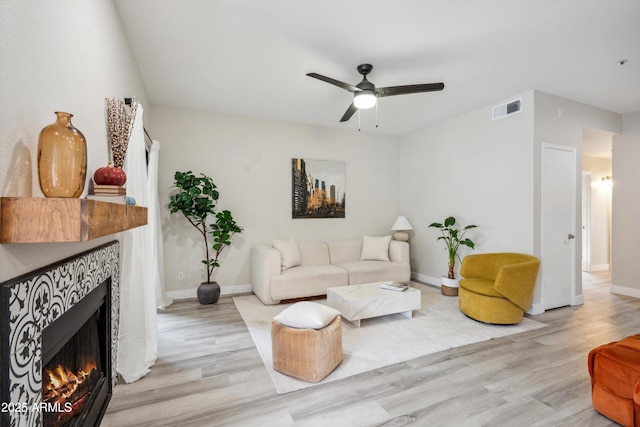 living room featuring wood finished floors, ceiling fan, a tiled fireplace, and baseboards