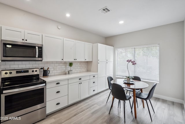 kitchen with stainless steel appliances, white cabinetry, backsplash, light countertops, and light wood-type flooring