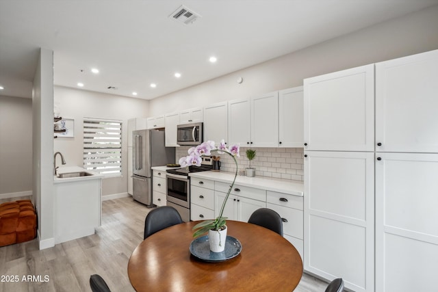 kitchen featuring stainless steel appliances, a sink, light countertops, white cabinets, and recessed lighting