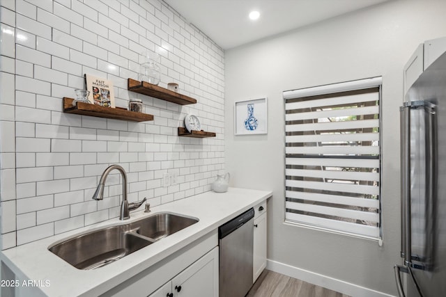 kitchen with a sink, stainless steel appliances, light wood-style flooring, light countertops, and tasteful backsplash