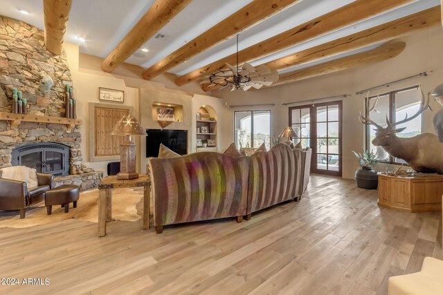 living room with ceiling fan, a stone fireplace, light wood-type flooring, and beam ceiling