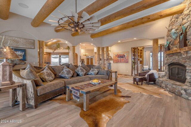 living room featuring light hardwood / wood-style flooring, ceiling fan with notable chandelier, a wealth of natural light, and a stone fireplace