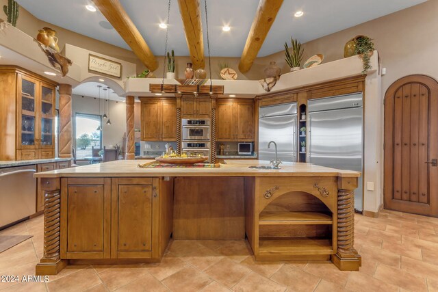 kitchen with beamed ceiling, stainless steel appliances, an island with sink, and sink