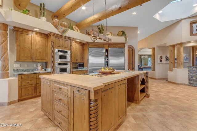 kitchen featuring a skylight, appliances with stainless steel finishes, a kitchen island with sink, beam ceiling, and butcher block counters