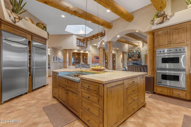 kitchen with beamed ceiling, a kitchen island with sink, stainless steel appliances, sink, and a skylight