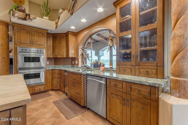 kitchen with light stone counters, light tile patterned flooring, stainless steel appliances, and sink