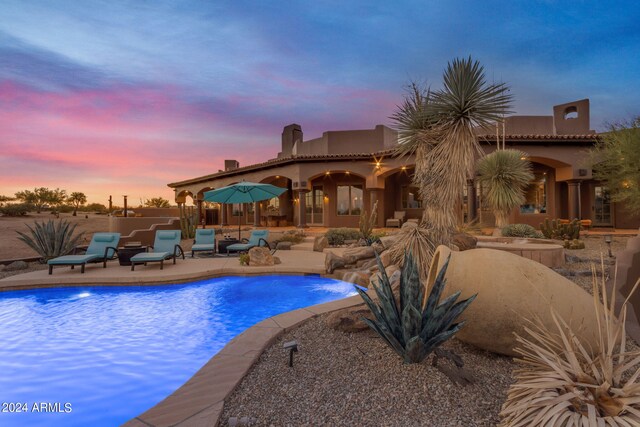 pool at dusk featuring a patio and pool water feature