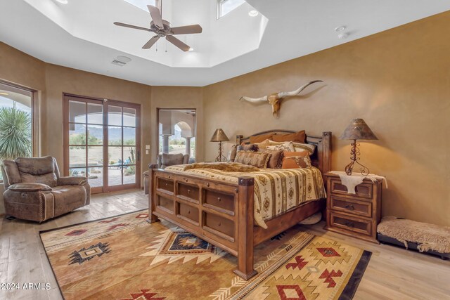 bedroom featuring light wood-type flooring, a tray ceiling, ceiling fan, and access to outside