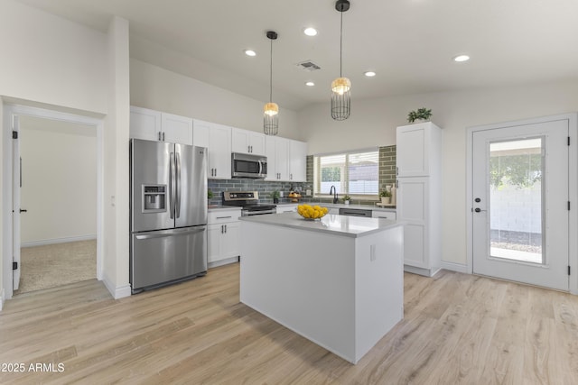 kitchen featuring tasteful backsplash, stainless steel appliances, decorative light fixtures, white cabinetry, and a kitchen island