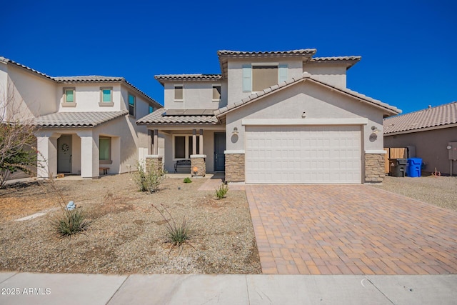 mediterranean / spanish-style home featuring decorative driveway, stucco siding, an attached garage, roof mounted solar panels, and stone siding