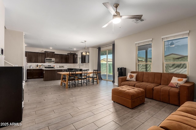 living room featuring a ceiling fan, visible vents, and light wood finished floors