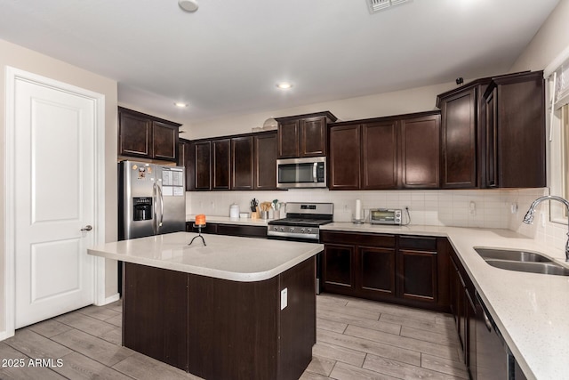 kitchen with dark brown cabinetry, tasteful backsplash, wood tiled floor, stainless steel appliances, and a sink