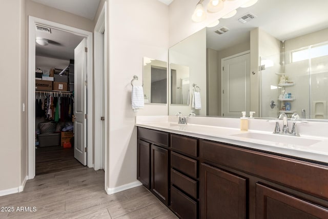 full bathroom featuring wood finished floors, a sink, visible vents, double vanity, and a stall shower