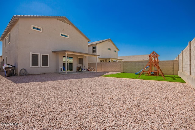 rear view of property with a playground, a fenced backyard, a yard, stucco siding, and a patio area