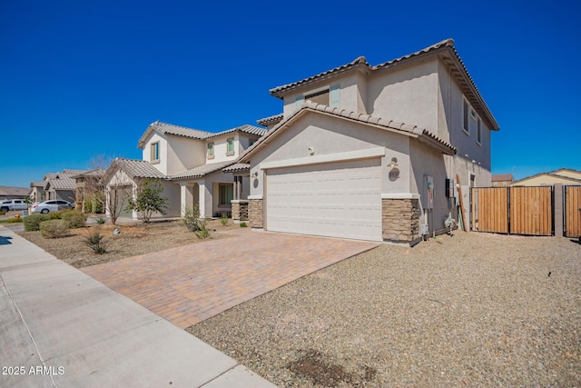 mediterranean / spanish home with a garage, fence, stone siding, decorative driveway, and stucco siding